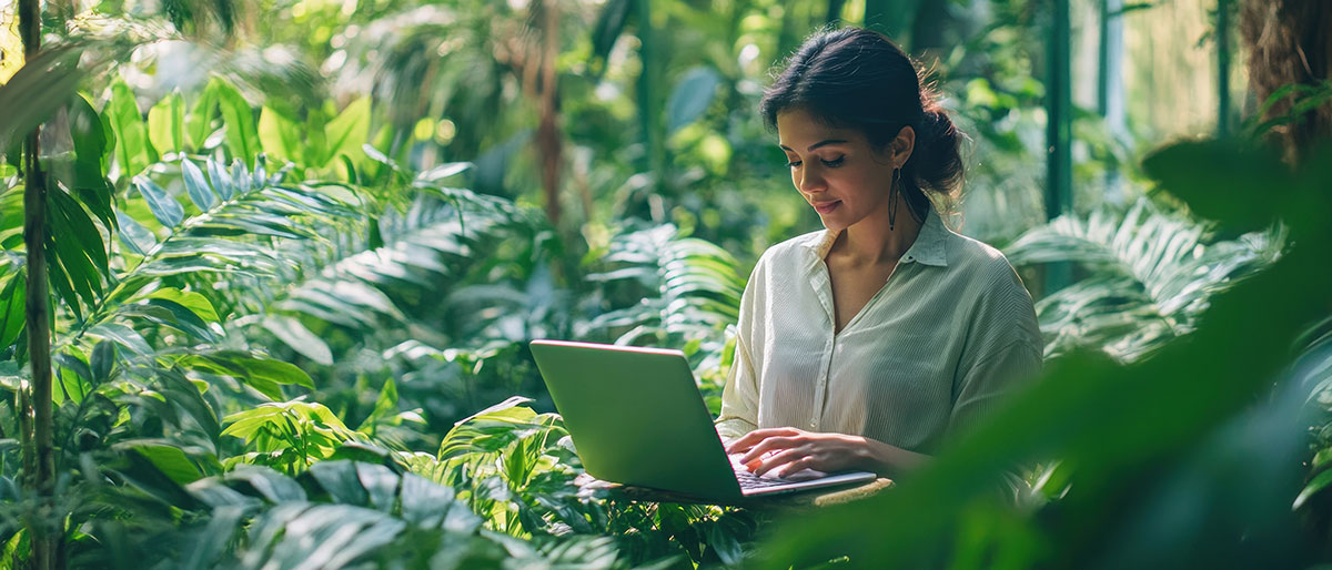 A young woman writing in her laptop surrounding of plants