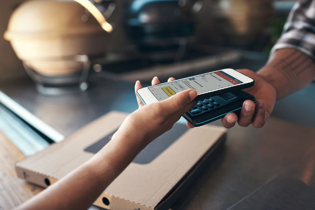 A woman's hand holding a smartphone placed on a small dataphone held by a man's hand